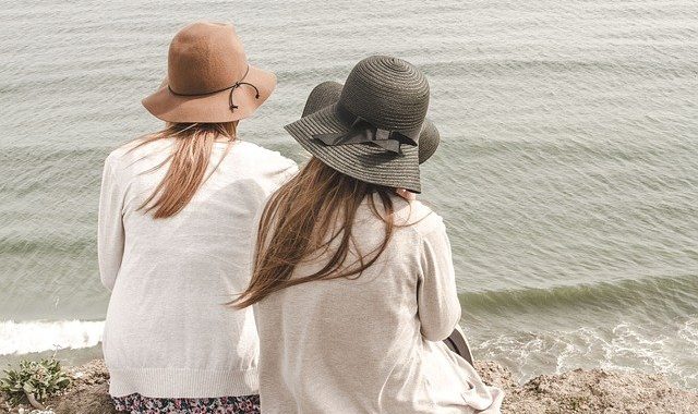 two women wearing sun hats look at the water